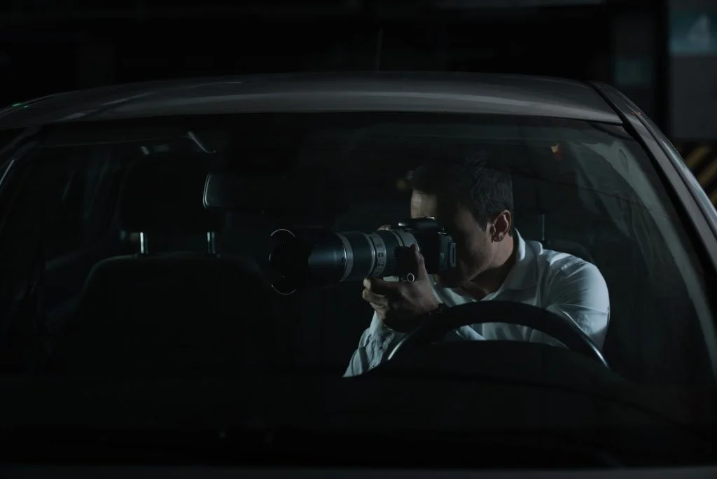 male private detective spying by camera with object glass from his car